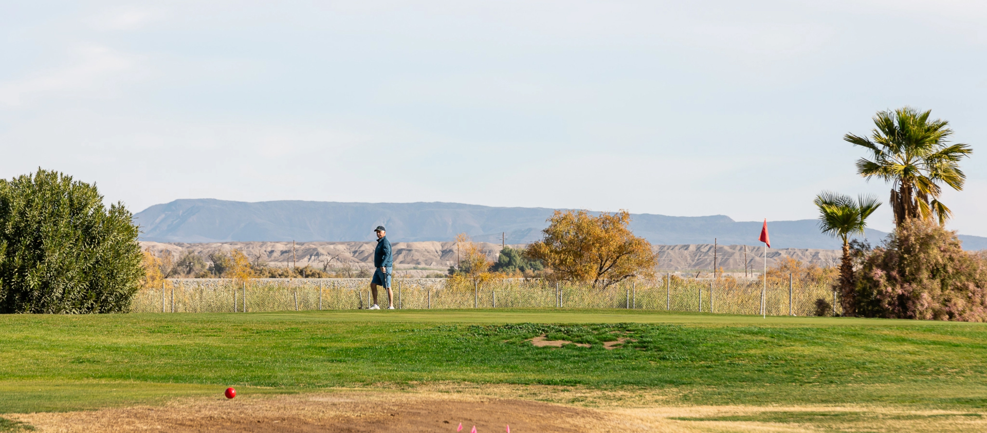 A golfer in shorts and a jacket walking along a green with gorgeous southwest Arizona scenery in the background.